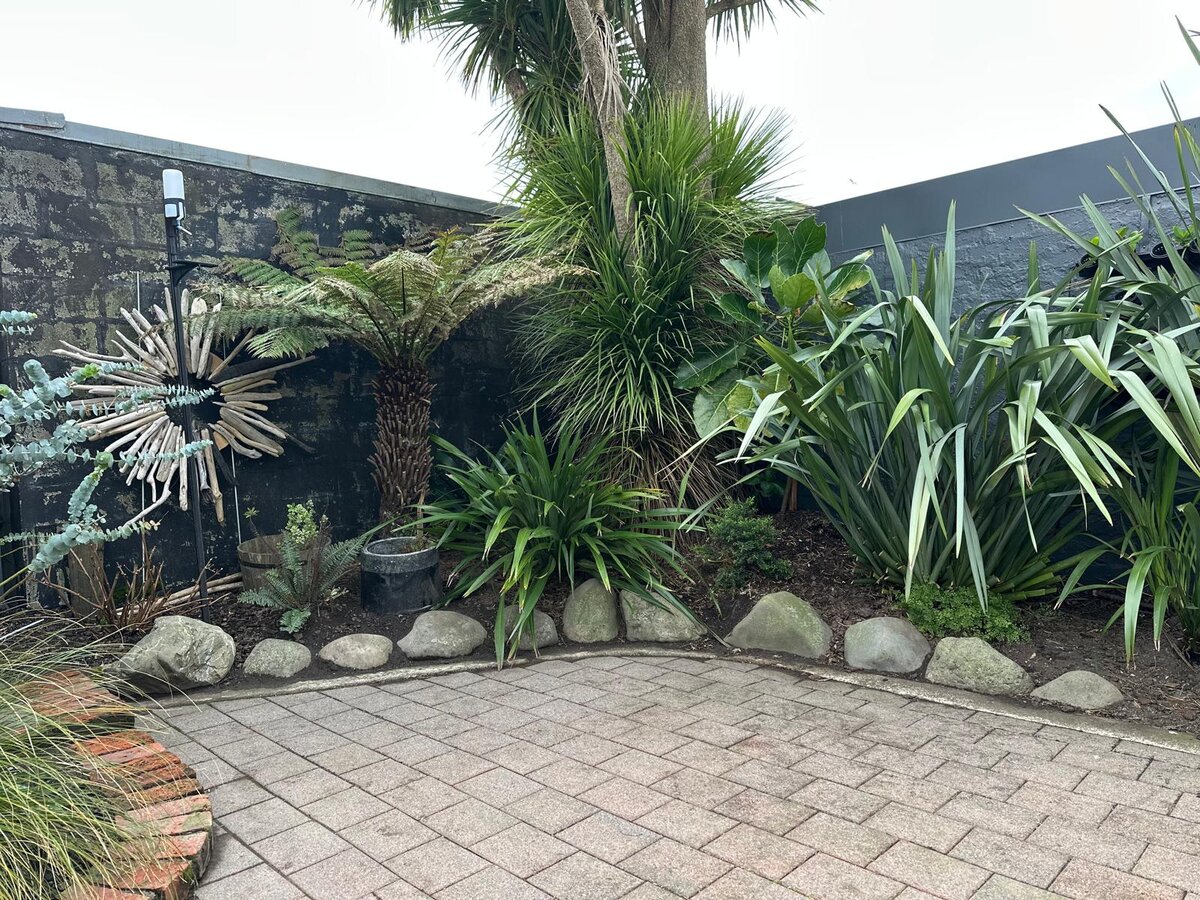Tidy paved backyard corner with fresh brick edging, rock border and lush established planting