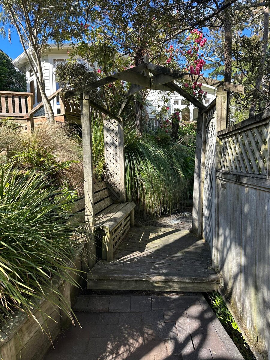 Wooden pergola archway and bench leading into a lush native garden path in Wadestown